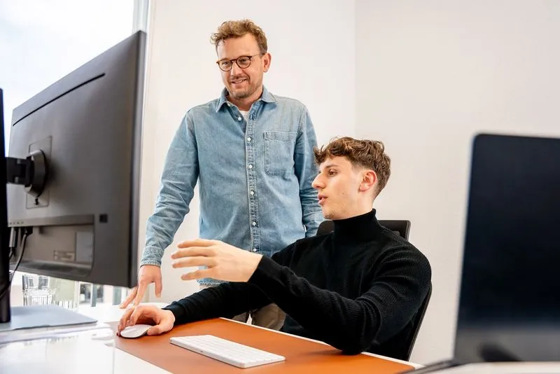 Two colleagues are discussing a project on screen in the Rügamer & Steiner office